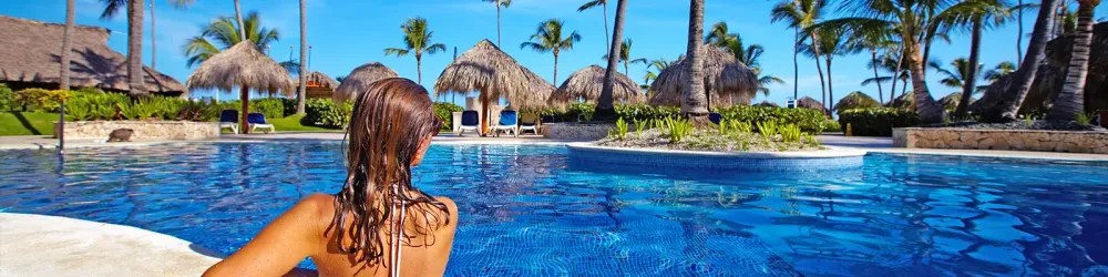 Woman in pool surrounded by palm trees and umbrellas